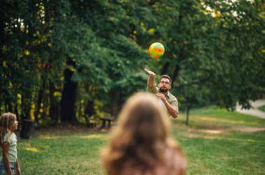 Aktif bir aile, doğada bir günü bir topla yazı tura oyunu oynayarak geçirir. Sportif bir baba, güneşli bir yaz gününde ailesiyle birlikte ormanın yakınındaki çayırda oyun oynuyor. Boşluğu kopyala.