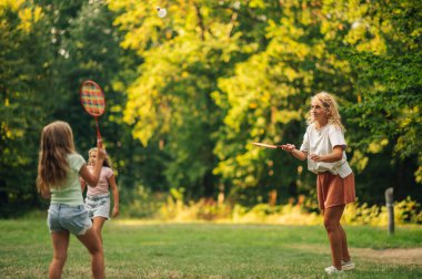 Güneşli bir yaz gününde doğada voleybol oynayan aktif bir anne ve kız. Sportif aile spor gününü ormanın yakınındaki çayırda badminton oynayarak geçiriyor. Aile badminton oynuyor..