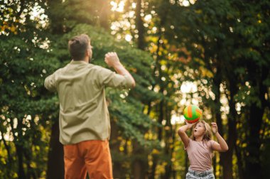 Sportif kız ve baba, doğada güneşli bir yaz gününde voleybol oynarken eğleniyorlar. Bir kız topa vuruyor. Sportif bir aile spor gününü doğada top oynayarak geçiriyor. Babalar Günü..