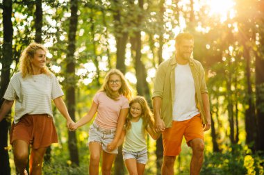 Vahşi doğayı keşfederken el ele tutuşan ve ormanda yürüyüş yapan mutlu bir ailenin portresi. Maceracı bir aile el ele tutuşup doğa yürüyüşü yaparken ormanı keşfediyor. Ormandaki aile.
