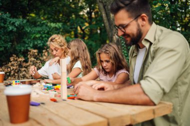 Piknik masasında oyun oynayan mutlu bir aile. İki takım ahşap bloklardan kuleler inşa etmek ve gülümsemek için yarışıyor. Eğlenceli bir aile piknik masasında masa oyunu oynuyor..