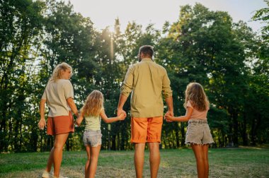 Sevecen, maceraperest bir ailenin el ele tutuşup doğayı keşfederken ormana doğru yürüyüşünün arka planında. Explorer ailesi birlikte doğa yürüyüşü yapıyor. Ebeveynler kızlarıyla el ele tutuşuyor.