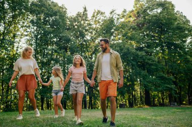 Dört kişilik neşeli bir aile el ele tutuşuyor ve doğa yürüyüşüne çıkıyorlar. Sevecen anne ve baba güneşli bir yaz gününü doğada geçiriyorlar ve dışarıdaki doğal güzellikleri keşfediyorlar. Boşluğu kopyala.