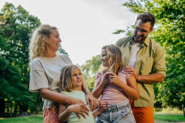 Sevecen dört kişilik bir aile doğada duruyor ve sarılıyor. Doğada dikilen ve birlikte eğlenen neşeli bir ailenin portresi. Doğada çocuklarla birlikte duran ebeveynlerin aile portresi.