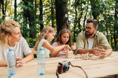 Sevgi dolu bir aile piknik masasında birlikte oturup jenga oynuyor. Kızlar ahşap bir yapboz kulesi inşa ederken aileler konuşuyor ve birlikte vakit geçiriyorlar..