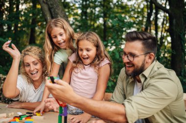 Neşeli mutlu bir aile doğada masada oturup eğlenceli bir masa oyunu oynuyor. Aile gülerken ve birlikte harika vakit geçirirken bir ahşap kiremit yapısı çöküyor. Eğlenceli oyun zamanı..