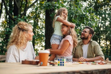 Sevecen kız kardeşler piknikte aileleri onlara bakarken birbirlerine sarılıyorlar. Doğada eğlenceli bir aile zamanı. Dört kişilik aile doğada kaliteli zaman geçiriyor. Aşk, bağlılık, şefkat konsepti.