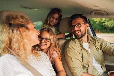 Yeni bir araba kullanan ya da şehirde test sürüşü yapan mutlu bir beyaz ailenin portresi. Ebeveynler ve kızları tatili otomobille seyahat ederek ve yolculuğun tadını çıkararak geçiriyorlar. Boşluğu kopyala.
