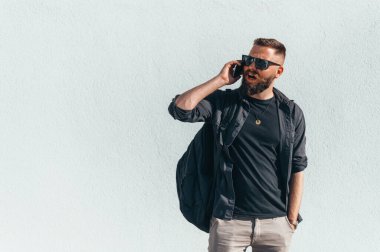 Beyaz bir duvarın önünde dururken akıllı telefon kullanan genç ve yakışıklı bir adam.