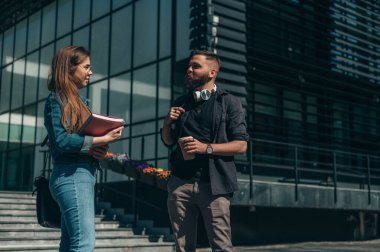 Fakültenin önünde toplanan iki genç öğrenci sabah dersleri için kitap ve kahve servisi yapıyorlar.