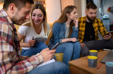 Bir grup genç öğrenci evde sınavlarına çalışırken ve kahve içerken zeka küpü kullanıyor.