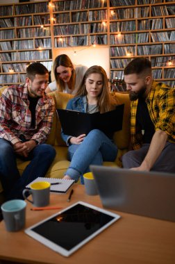 Genç bir grup öğrenci evde dizüstü bilgisayar kullanırken, kitap okurken ve sınavlarına hazırlanırken birlikte okuyorlar.