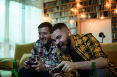 En iyi iki arkadaş evde kanepede oturup bira içerken video oyunu oynuyorlar.