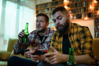 En iyi iki arkadaş evde kanepede oturup bira içerken video oyunu oynuyorlar.