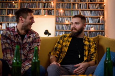 Bir grup arkadaş ev partisinde bira içerken ve kanepede birlikte otururken eğleniyorlar.