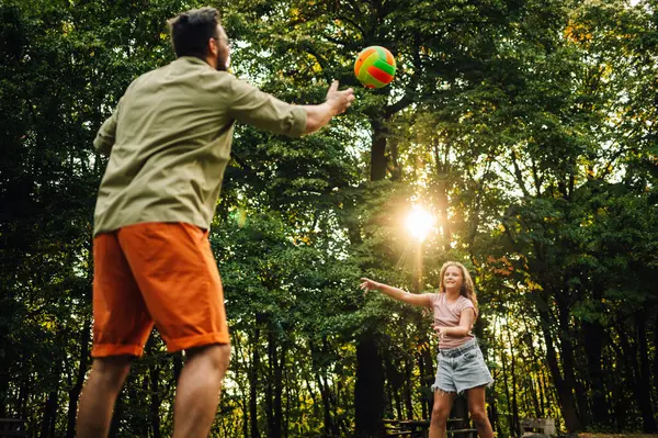 Doğada orman yakınlarında voleybol oynayan sportif bir baba ve kızın düşük açılı görüntüsü. Spor yaparken kendilerini eğlendiren aktif bir aile. Doğada eğlence. Aile içinde aile