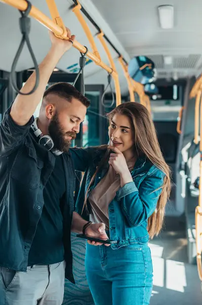 Güzel bir çift hareket halindeki bir otobüste duruyor ve akıllı telefon kullanırken konuşup flört ediyorlar.
