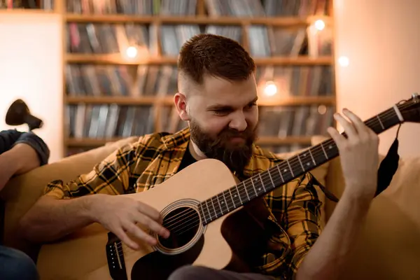 Evde dinlenirken gitar çalan ve ruhuna uygun müzik çalan tutkulu genç bir adam.