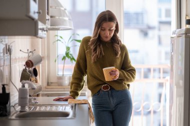 Genç ve mutlu bir kadın sabahları mutfakta kahve içiyor. Çekici bayan evde çay içmekten zevk alıyor.