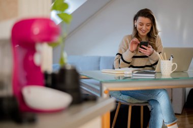 Çekici bir kadın ara veriyor ve evinde dizüstü bilgisayarla çalışırken internette sörf yaptığı için elinde akıllı telefon tutuyor..