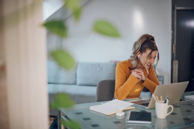 Genç bir kadın laptopunu kullanıyor ve iş arkadaşlarıyla evden iş yaparken görüntülü görüşme yapıyor. Webinar 'ı dinlemek. E- posta Denetiliyor