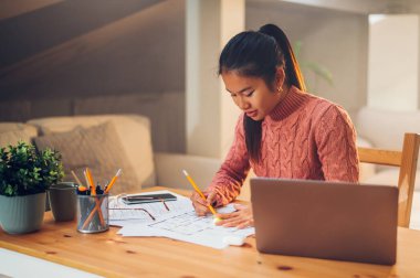 Gülümseyen Asyalı kadın portresi evde oturuyor ve bir dizüstü bilgisayarla çalışıyor ya da çalışıyor. Genç Vietnamlı kadın bilgisayar kullanıyor ve evrak işleriyle uğraşıyor. Boşluğu kopyala.