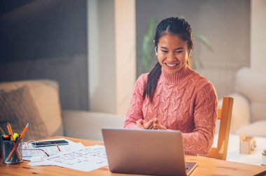 Gülümseyen Asyalı kadın dizüstü bilgisayara bakıyor ve e-posta okuyor, video izliyor, sosyal ağda sohbet ediyor ya da evde online alışveriş yapıyor. Kirayı, faturaları, benzini ve elektriği internet üzerinden ödemek için teknoloji kullanılıyor.