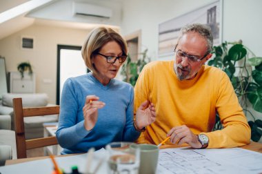 Masada oturup notlar alırken yeni bir ev için plan yapan evli bir çift. İpotek kredisi yatırımı ve inşaat konsepti planı. Ev planları..