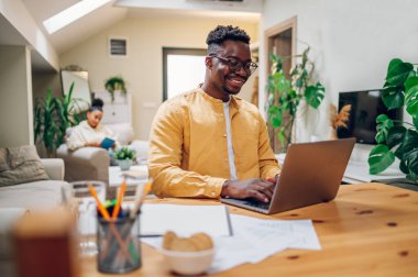 Afrika kökenli Amerikalı bir adam evinde oturmuş, aylık aile bütçesini hesaplarken bir yandan da belge ve dizüstü bilgisayar kullanıyor. Alışveriş masrafları, elektrik faturaları, online bankacılık uygulaması.