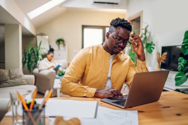 Afro-Amerikan bir adamın portresi dizüstü bilgisayara bakıyor ve sorunları çözerken ve finansal bir plan yaparken geleceği planlıyor. Çevrimiçi bankacılık, abuk sabuk konuşmalar ve faturalar. Baş ağrısı ve stres.
