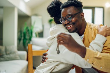 Çok ırklı bir çift yeni evlerinin anahtarlarını tutuyor ve neşeyle sarılıyorlar. Yeni eve yatırım yapmak. Finansal strateji ve plan yapıyorum. Birçok çift aynı eve taşınıyor. Boşluğu kopyala.