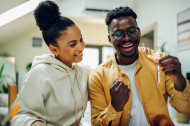 Yeni evlerinin anahtarlarını tutarken ve kutlama yaparken gülümseyen çok ırklı bir çift. Yeni eve yatırım yapmak. Finansal strateji ve plan yapıyorum. Çeşitli mülk sahipleri. Boşluğu kopyala.