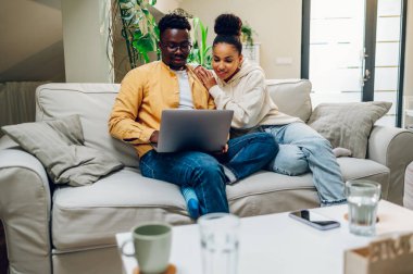 Genç, çok ırklı bir çift evdeki kanepede dizüstü bilgisayar kullanırken dinleniyor. Afrikalı Amerikalı erkek ve İspanyol kadın film izliyor ya da internette geziniyorlar. Aşk, mutluluk, insanlar ve eğlence konsepti.