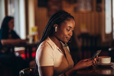 Güzel Afro-Amerikalı kadın bir kafede oturup kahve içerken akıllı telefon ve uçak kullanıyor.