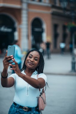 Güzel Afrikalı Amerikalı kadın şehir turu sırasında akıllı telefonuyla selfie çekiyor.