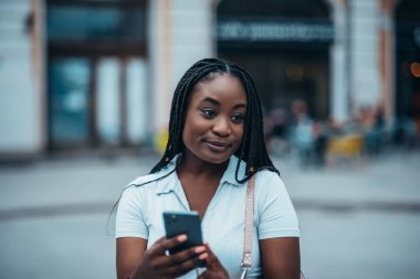 Neşeli Afrikalı Amerikalı kadın şehir dışındayken akıllı telefon kullanıyor.