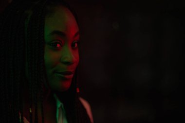 Yeşil ve kırmızı ışıkla aydınlatılırken karanlıkta poz veren güzel bir Afrikalı Amerikalı kadının portresi.