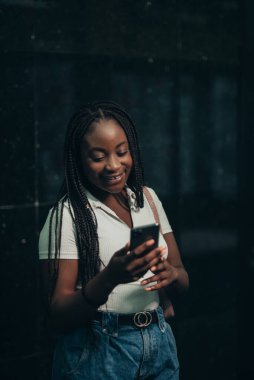 Neşeli Afrikalı Amerikalı kadın gece metro istasyonunda akıllı telefon kullanıyor.