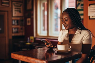 Güzel Afrikalı Amerikalı kadın bir kafede espresso içerken akıllı telefon kullanıyor.