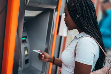 Neşeli Afrikalı Amerikalı kadın kredi kartı kullanıyor ve ATM 'den para çekiyor.