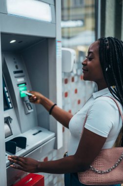 Neşeli Afrikalı Amerikalı kadın kredi kartı takıyor ve ATM 'den para çekiyor.