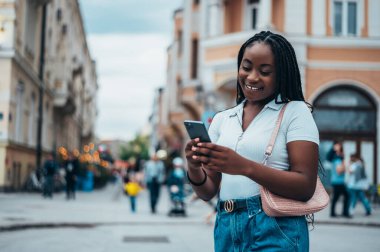Neşeli Afro-Amerikalı kadın şehir dışındayken akıllı telefon kullanıyor.