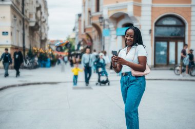 Neşeli Afrikalı Amerikalı kadın şehir dışındayken akıllı telefon kullanıyor.