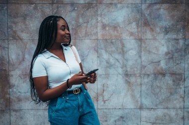 Neşeli Afrikalı Amerikalı kadın şehir dışındayken akıllı telefon kullanıyor.