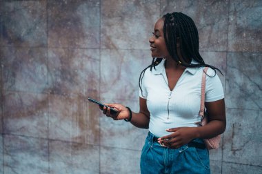 Neşeli Afrikalı Amerikalı kadın şehir dışındayken akıllı telefon kullanıyor.