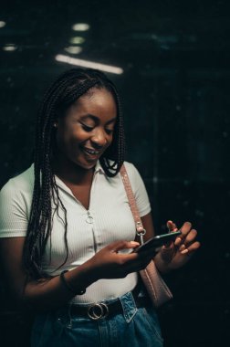 Güzel Afrikalı Amerikalı kadın metro istasyonunda toplu taşıma için beklerken akıllı telefon kullanıyor.