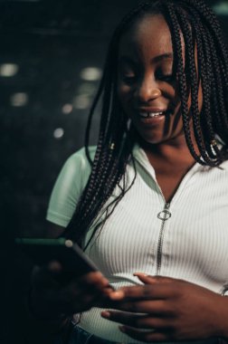 Güzel Afrikalı Amerikalı kadın akıllı telefon kullanıyor ve gülümsüyor.