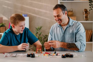 Küçük oyuncak parçaları birleştirirken, yemek masasında oynayan, gülümseyen sarışın bir çocukla sevgili babasını yakından çek. Hafta sonlarını birlikte geçirirken eğleniyorlar ve gülümsüyorlar..