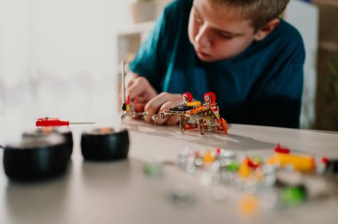 Arka plandaki çocuk oyuncağın diğer parçaları üzerinde çalışırken ve onları monte etmek için hazırlarken masanın üzerinde duran oyuncağı yakın plan çek. Hafta sonunu evde oynayarak ve eğlenerek geçirmek.