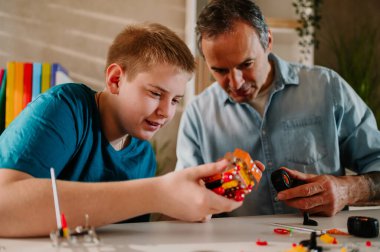 Babası ona yardım ederken gülümseyen genç bir çocuğun oyuncağı üzerinde çalışırken yakın çekim. Evde boş vakit geçirirken oyuncağı birleştirmek. Bir baba ve oğul arasındaki mutlu aile anları.